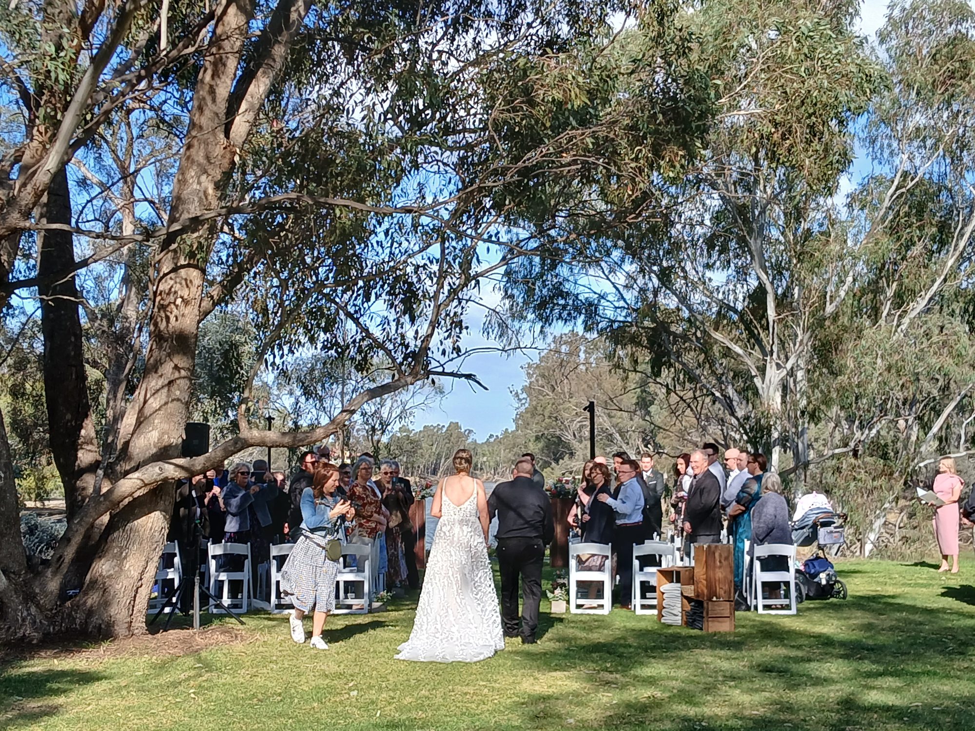 Bride walking down the aisle on the riverbank lawn under the gums