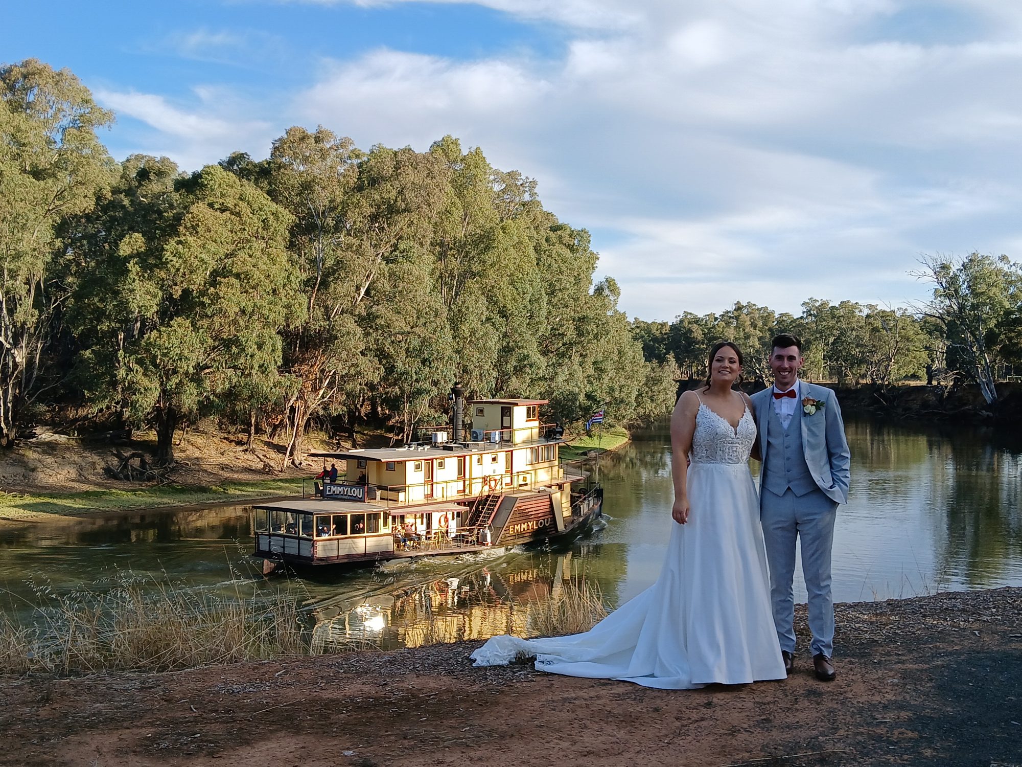 Newlyweds on the riverbank with a paddle steamer behind them