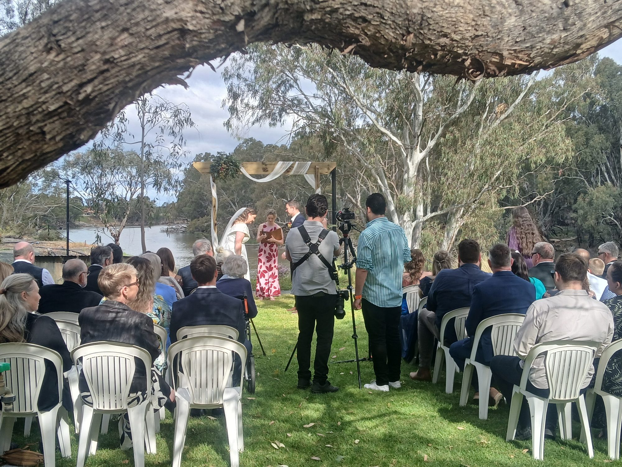 Riverbank ceremony beneath a large river red gum, the Murray behind the arch