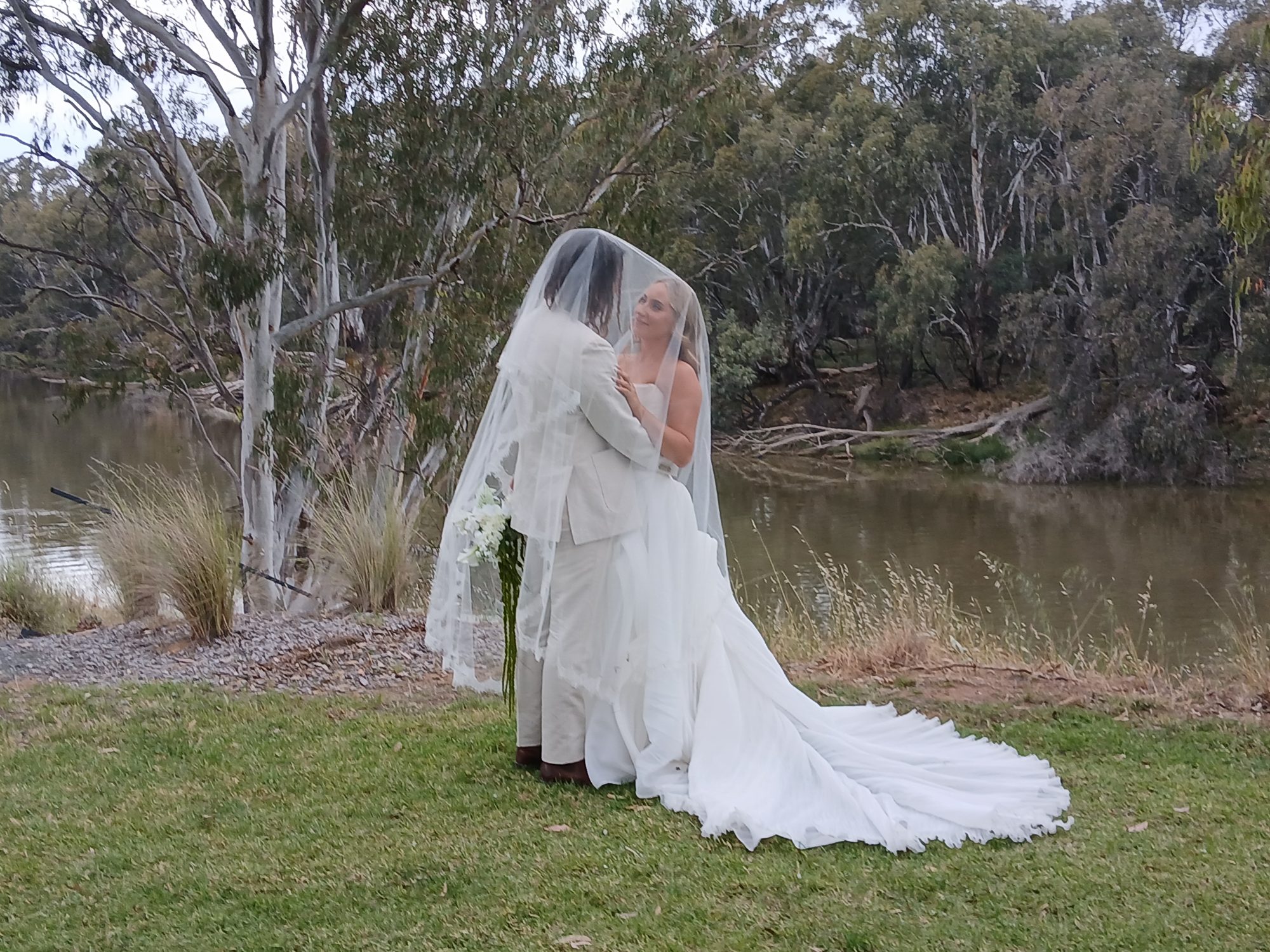 Couple beneath the veil on the riverbank lawn beside the Murray